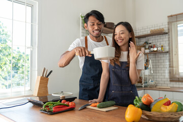 Young Asian couple in apron learning to choose ingredients Ingredients salad dressing in pot,...