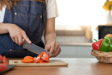 Beautiful Asian woman in kitchen cooking apron preparing various vegetable ingredients and slicing tomatoes in online cooking prep for the health and happiness of our loved ones in their own homes.