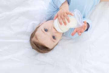 baby boy eats milk from a bottle on the bed before going to bed in a blue bodysuit, baby food concept