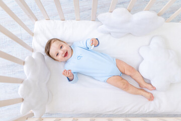 happy smiling baby boy in crib in blue bodysuit, cute joyful little baby in bedroom