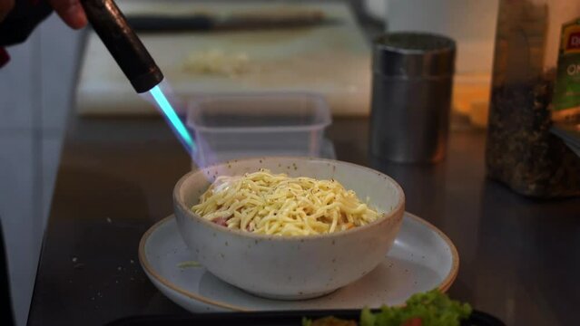 Professional chef use butane torch to burn and melt the cheddar on top of a bowl of delicious and tasty macaroni and cheese, adults and kids favourite comfort food, close up shot.