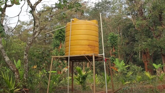 Bright yellow water tank on tower with green forest background. Well storage provides water source for drinking, bathing, irrigation and life of rural farm in India.