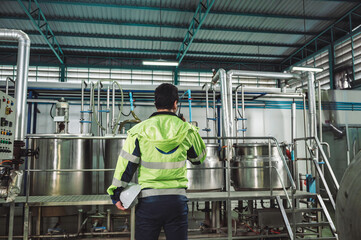 Caucasian technician engineer man in safety uniform standing with pipeline, boiler tank in beverage processing laboratory plant