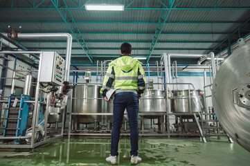 Caucasian technician engineer man in safety uniform standing with pipeline, boiler tank in beverage processing laboratory plant