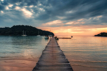 Sunset over wooden pier and boat in tropical sea at Koh Kood Island