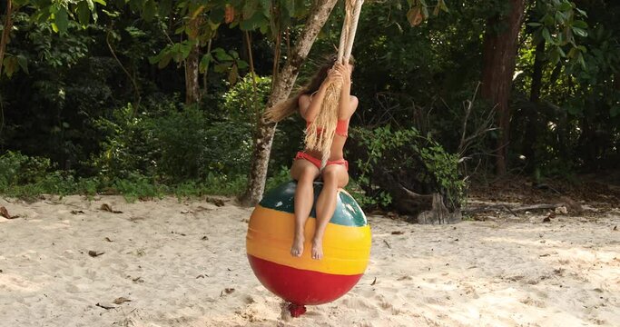 Woman swinging on swings made from old buoy on the beach