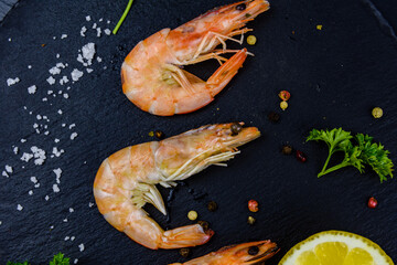 Shrimps with spices, salt, lemon and parsley on a slate board. Top view
