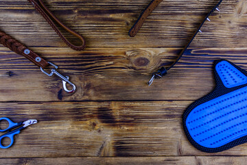 Brown leather dog leash, collar, pet slicker brush glove and scissors for claws on a wooden background. Top view