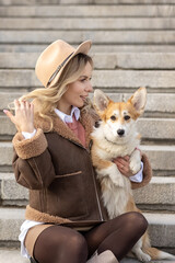 A young blonde woman in a hat on a walk in the park with Welsh Corgi-Pembroke dogs.Spring