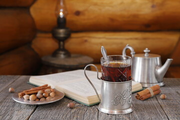 On wooden table on background of old lantern standing on wooden barrel near log wall is glass of...