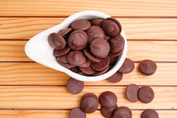 A group of dark brown buttons in a small white bowl on a wooden table