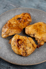 Chicken breasts barbecued and served on the blue plate above dark moody background