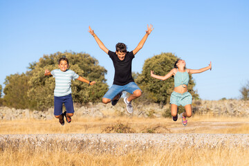 Three funny kids jumping on a field on a summer day