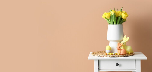 Vase with yellow tulips, Easter eggs and rabbits on table near beige wall. Banner for design