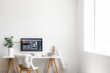 Modern workplace with computer and eucalyptus in vase near light wall