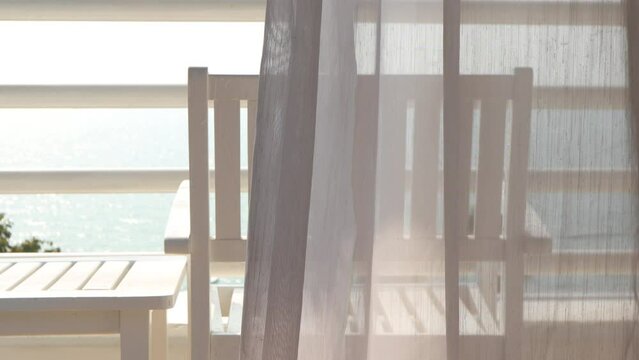 Empty white chair and transparent curtain on the door moved by the wind with sea beach outside view. Scenic relaxing scenery