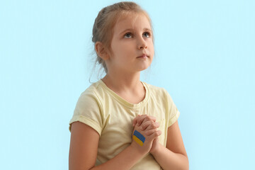 Little girl with drawn flag of Ukraine praying on blue background