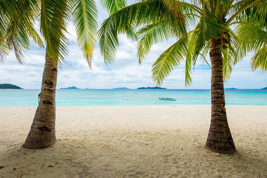 Palm trees and blue water on the white sand beach of Malcapuya Island