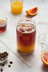 Bumble coffee, coffee cocktail with orange juice, syrup and ice in transparent jar-shaped glasses on a light background.