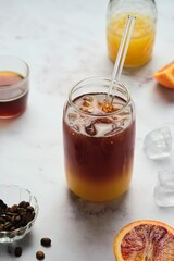 Bumble coffee, coffee cocktail with orange juice, syrup and ice in transparent jar-shaped glasses on a light background.