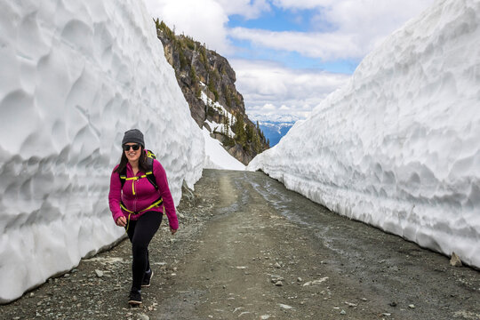 Woman hiking on road between snow walls, Whistler Blackcomb, Whistler, British Columbia, Canada