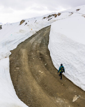 Woman hiking on road between snow walls, Whistler Blackcomb, Whistler, British Columbia, Canada