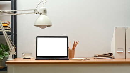 Laptop computer with white empty display, lamp, pencil holder and coffee cup on wooden office desk