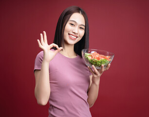 Young Asian woman eating salad on background