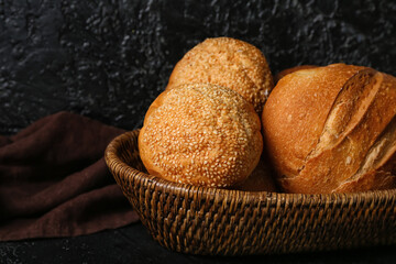 Wicker basket with loaves of different bread on black table