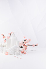 Cosmetic products for makeup, cleansing skin in white bottles, branch of spring pink sakura flowers, toiletry, elegant bathroom interior in geometric futuristic asian style, copy space, vertical.