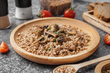 Wooden plate of tasty buckwheat porridge with mushrooms and dill on grey table