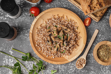 Wooden plate of tasty buckwheat porridge with mushrooms and dill on grey table