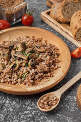 Wooden plate of tasty buckwheat porridge with mushrooms and dill on grey table