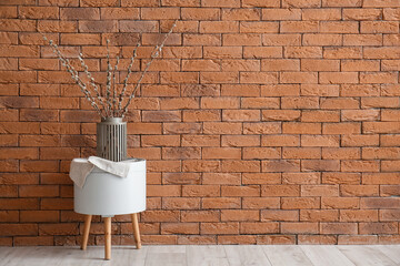 Vase with pussy willow branches on table near brick wall