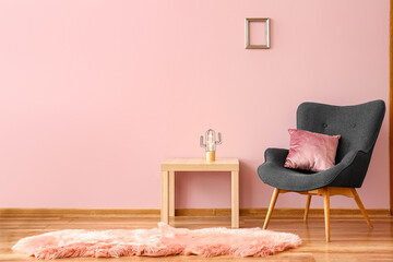 Stylish grey armchair with cushion, fur rug and table near pink wall