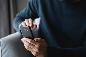 man using smartphone on sofa in living room at home, searching data and social media on internet.