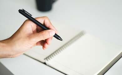left handed man holding a pen and writing in a notebook on the table