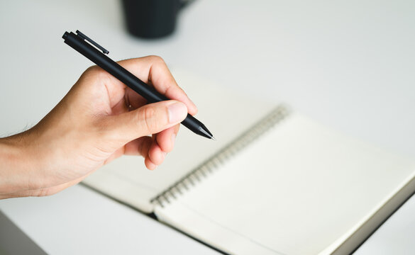 left handed man holding a pen and writing in a notebook on the table
