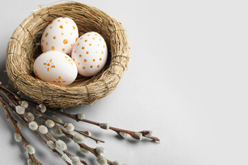 Nest with painted Easter eggs and willow branches on light background