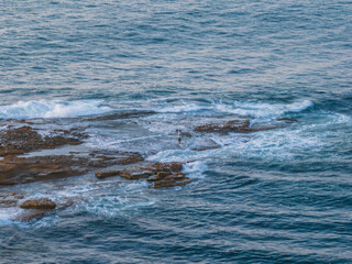 Rock fisherman on the rock ledge surrounded by the sea