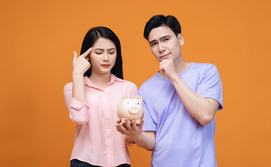 Young Asian couple holding piggy bank on background