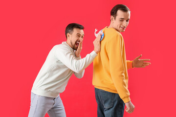Young man sticking paper on his friend's back against red background. April Fools' Day celebration