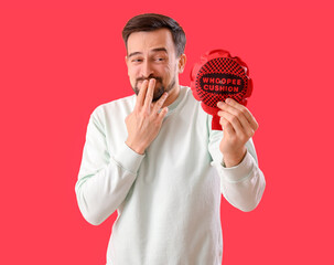 Handsome man with whoopee cushion laughing on red background. April Fools' Day celebration