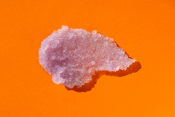 Sugar body scrub texture on orange background. Cosmetic smear. Appearance of the texture of the lilac swatch. Natural skincare products. Beauty concept for face and body care.