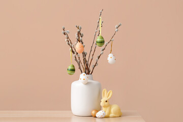 Vase with willow branches, Easter eggs and toy bunny on table near color wall