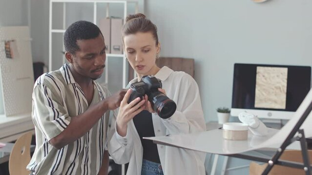 Medium slowmo of two multiethnic male and female photographers doing commercial still photography of cosmetic products in photo studio, photographing on professional digital camera