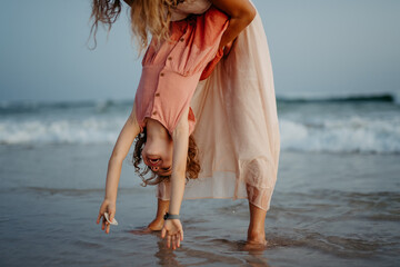 Mother holding her daughter upside down, enjoying summer vacation, having fun.