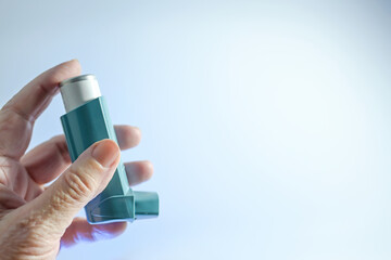 Old hand holding a meter-dosed inhaler, also known as pump or allergy spray, medical device for...