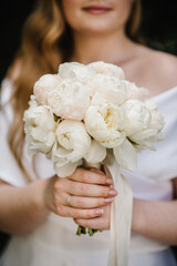 Obraz na płótnie Canvas A young girl is standing and holding a bouquet of white peonies with a ribbon at a wedding ceremony. Flowers close up. Engagement ring.