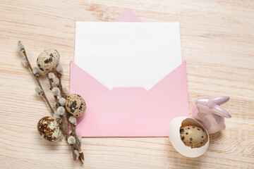 Envelope with blank greeting card, Easter eggs, bunny and pussy willow branches on wooden background